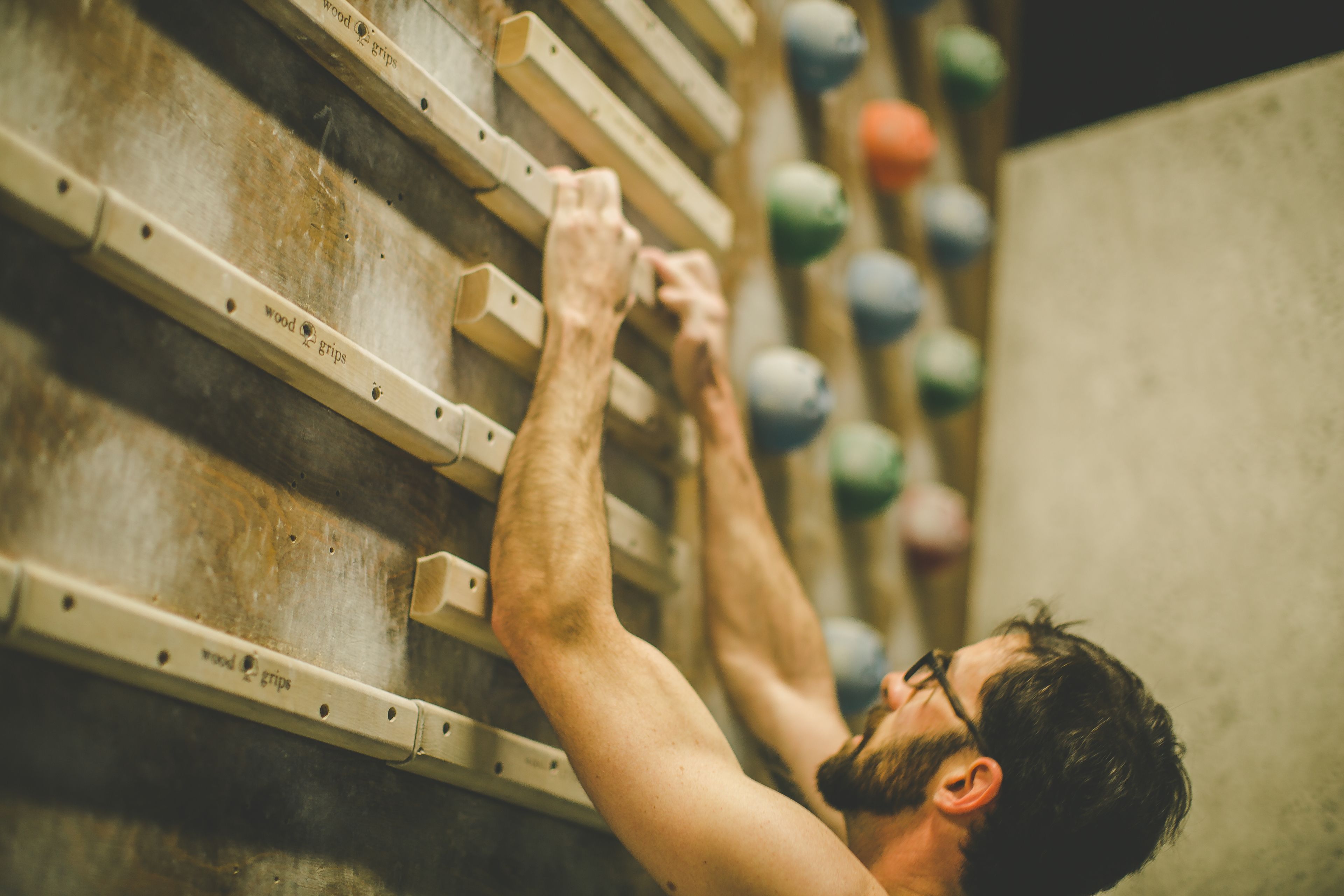A person climbing a wooden climbing wall with various colored holds.