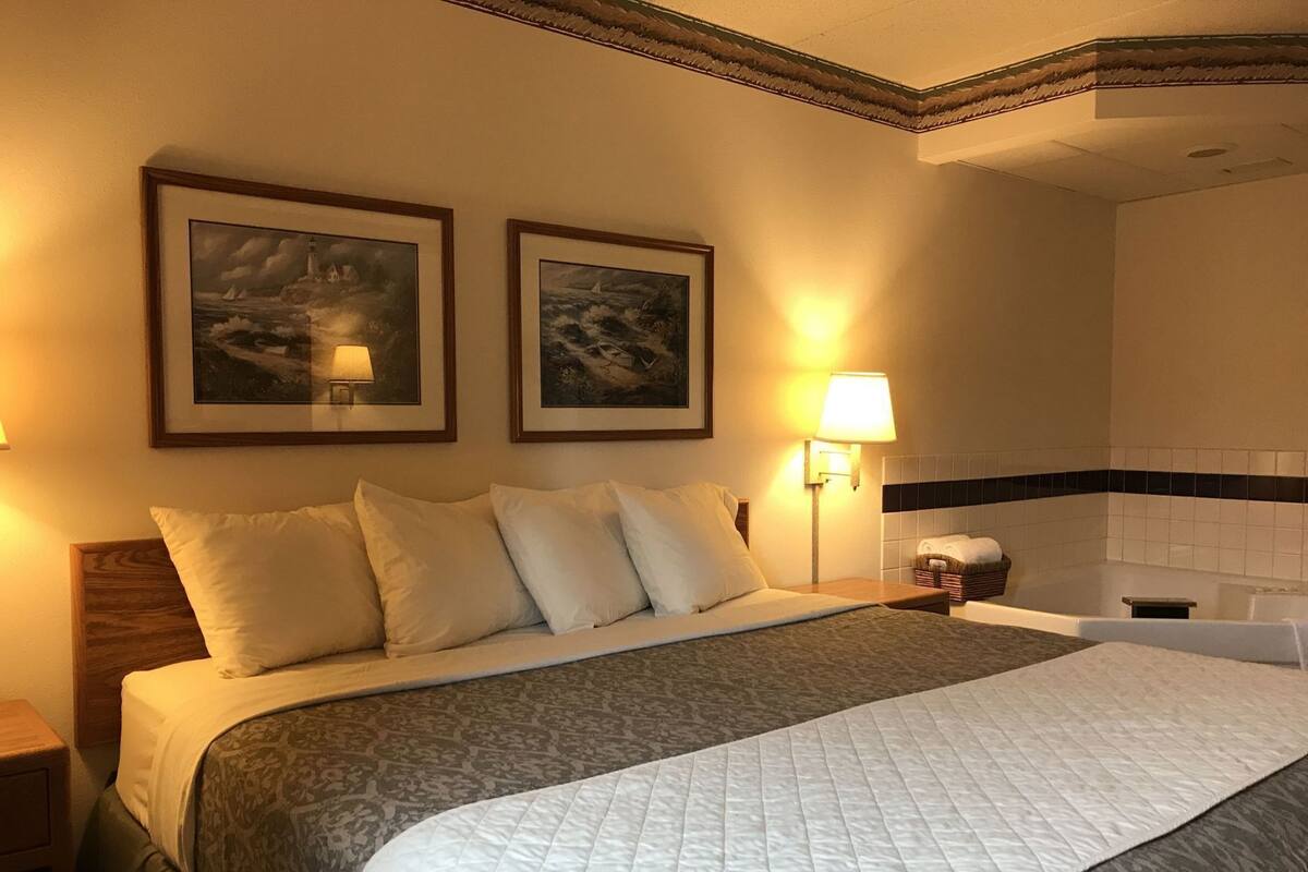 A hotel room with a bed, two wall-mounted lamps, a framed painting, and a bathtub.