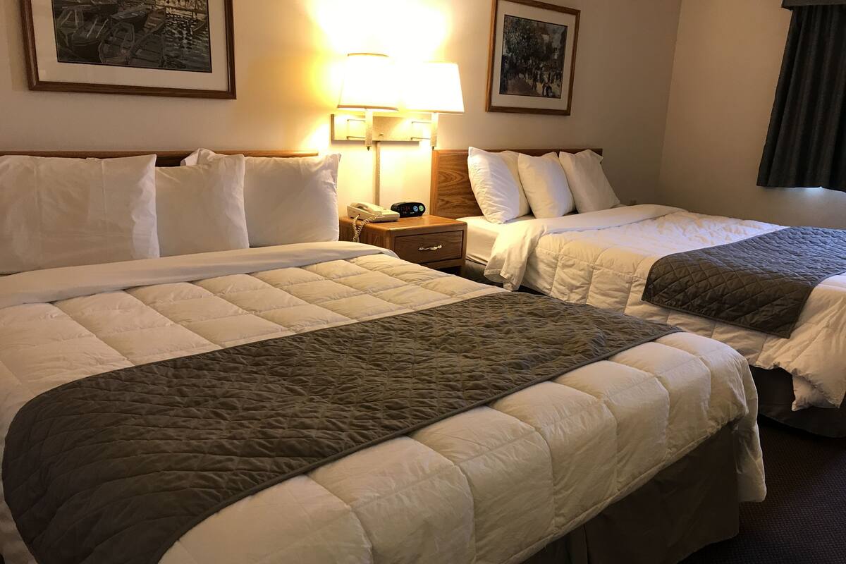 A hotel room with two beds, a bedside table with a lamp, and a framed picture on the wall.