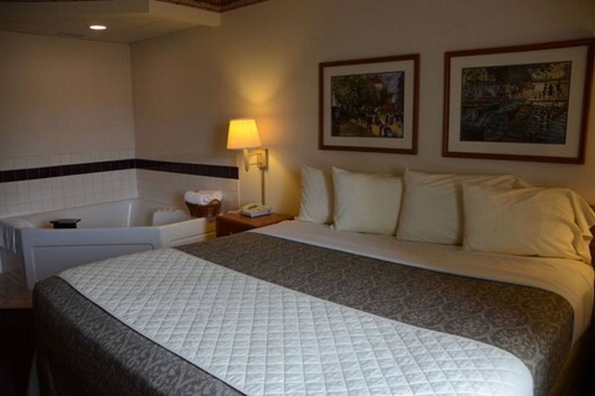 A hotel room with a bed, a nightstand, a lamp, a bathtub, and two framed pictures on the wall.