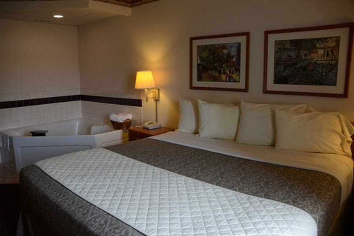 A hotel room with a large bed, a bathtub, and two framed pictures on the wall.