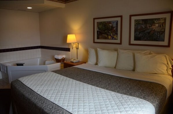 A hotel room with a large bed, a bathtub, and two framed pictures on the wall.