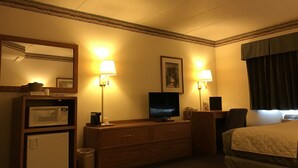 A hotel room with a bed, a TV, a desk with a lamp, a microwave, and a trash can.
