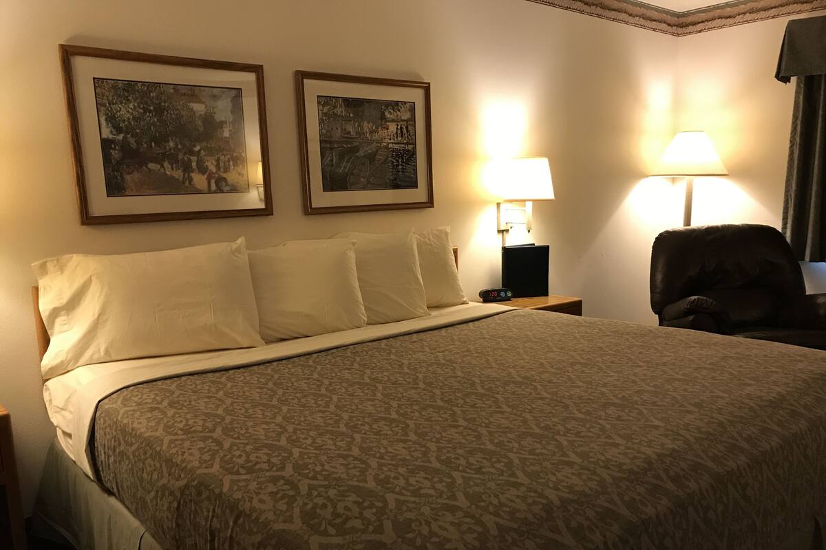 A hotel room with a large bed, two bedside lamps, and two framed pictures on the wall.