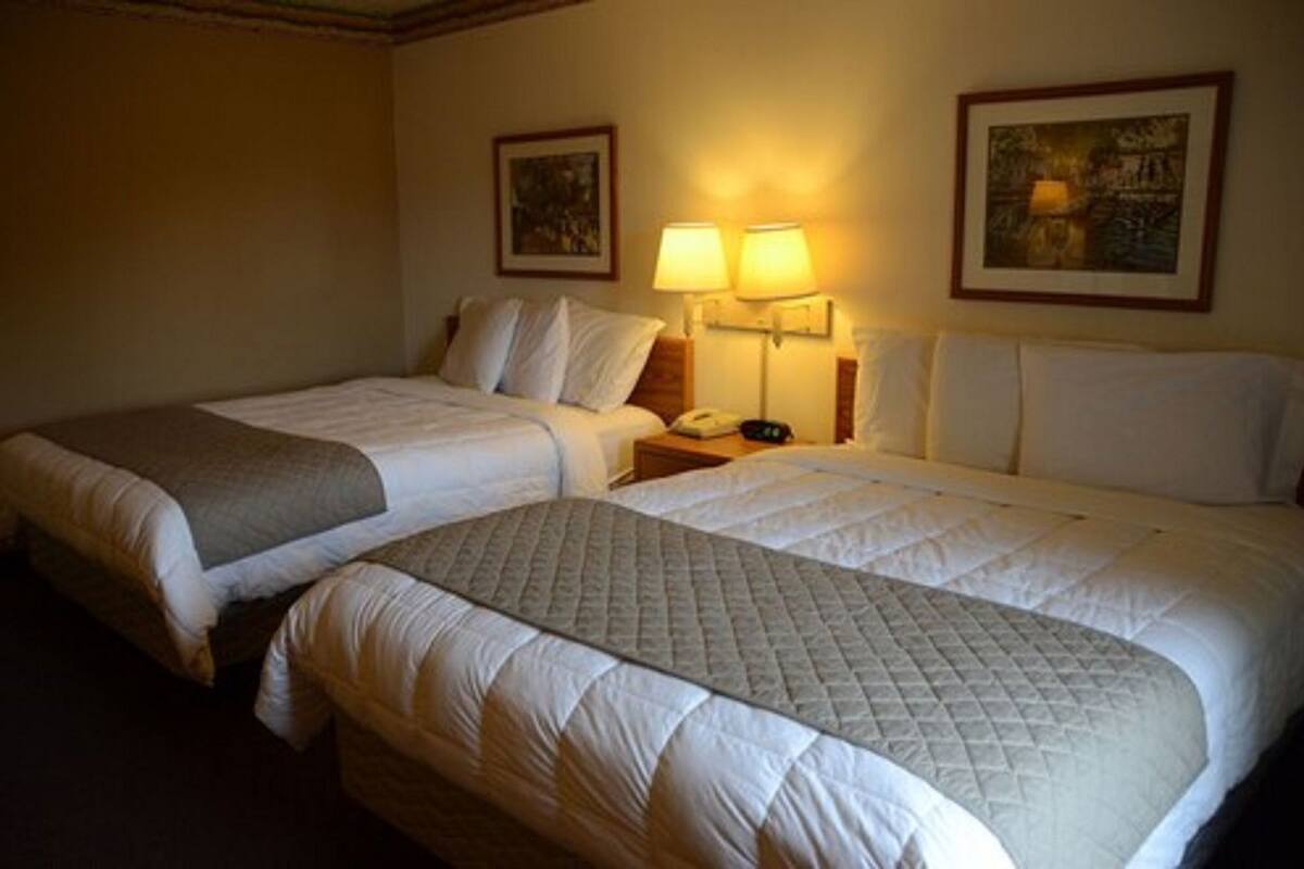 A hotel room with two beds, a nightstand with a lamp, and two framed pictures on the wall.