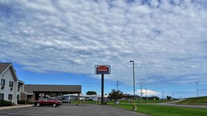 A Fairbridge Inn & Suites with a parking lot, a building with a sloped roof, and a grassy area in the background.