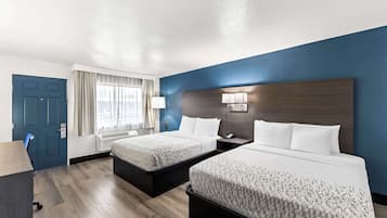 A hotel room with two beds, a desk, and a chair.