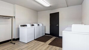Une buanderie équipée de quatre machines à laver blanches, d’un étendoir métallique et d’une porte noire.