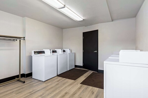 A laundry room with four white washing machines, a metal drying rack, and a black door.