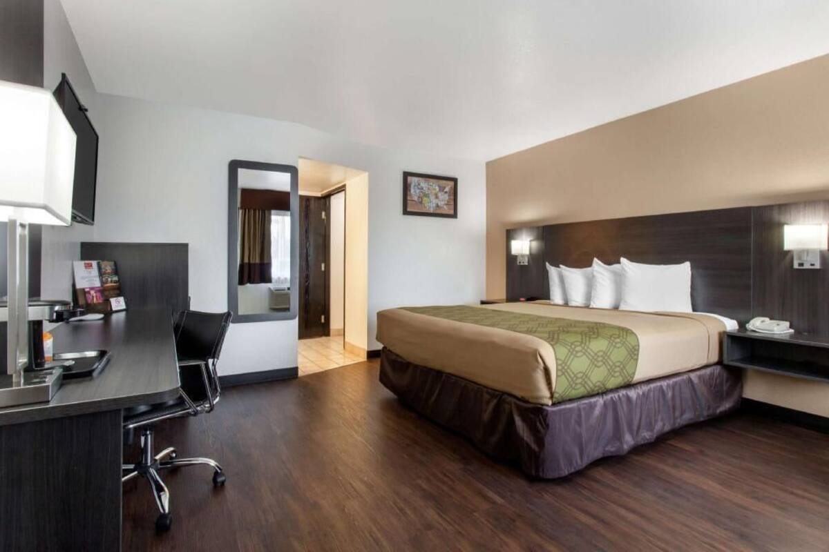 Ein Hotelzimmer mit Bett, Schreibtisch, Stuhl und einer Tür zu einem anderen Raum.