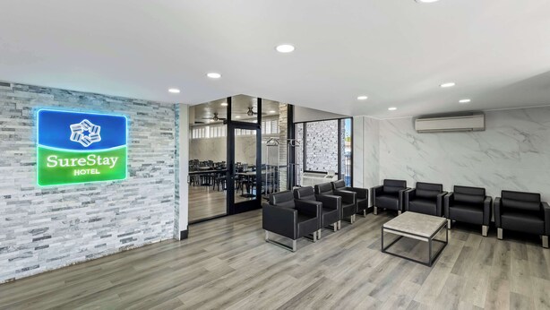 Un hall d'accueil d'hôtel avec une enseigne « SureStay Hotel », un coin salon avec des chaises noires, une table basse en bois et un mur en marbre.