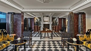 A lobby with a checkered floor, marble columns, and a fireplace.