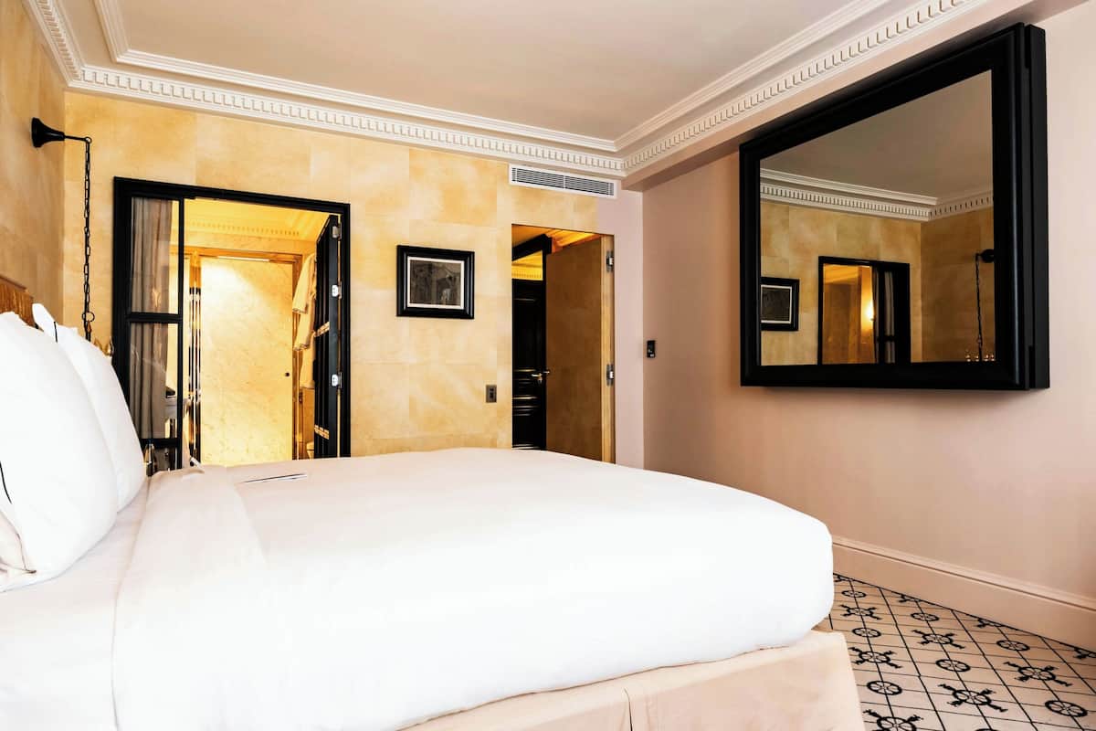 A hotel room with a large bed, a mirror, and a door leading to another room.