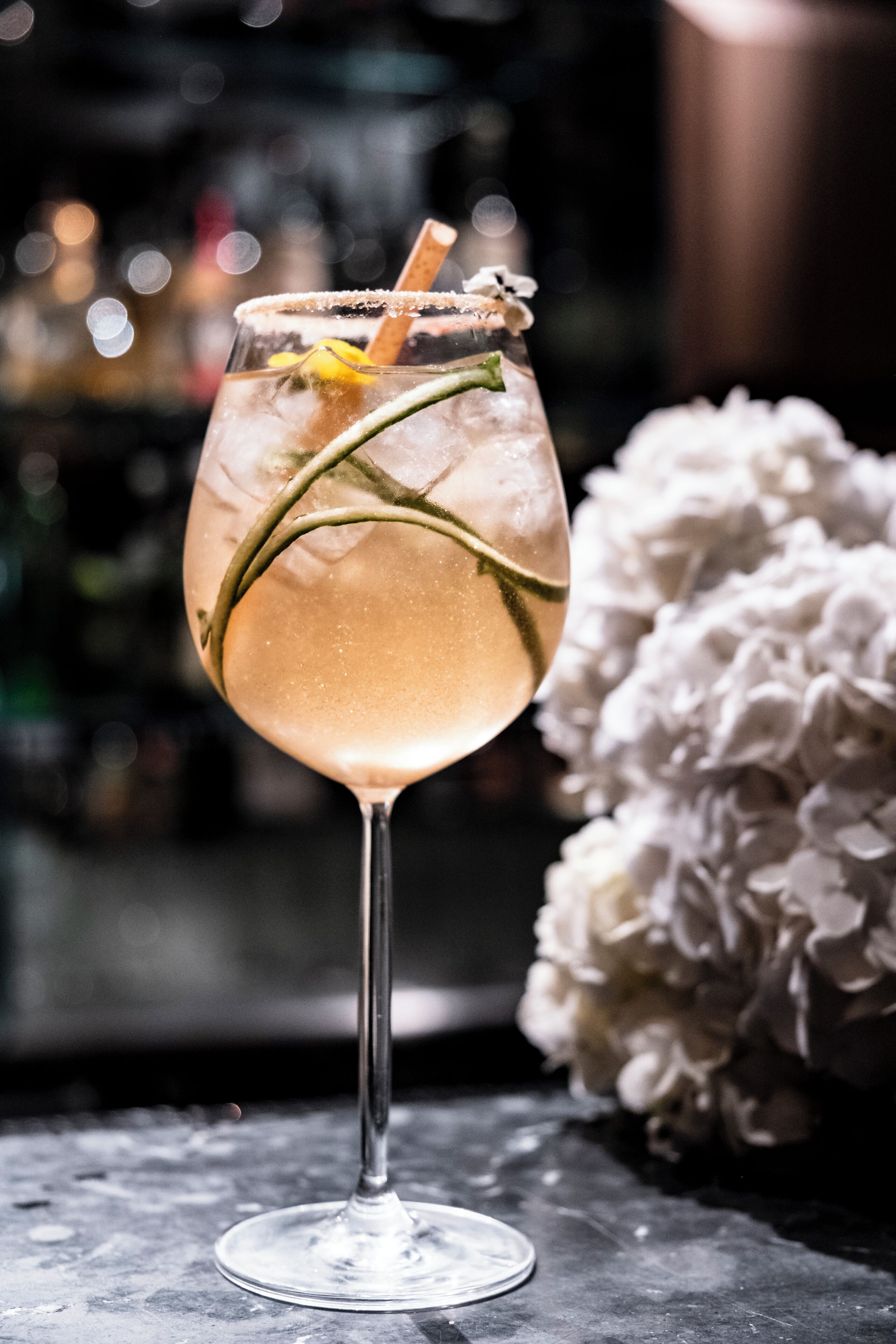 Een cocktailglas met rietje, versierd met een bloem en een groen blad, op een marmeren oppervlak.