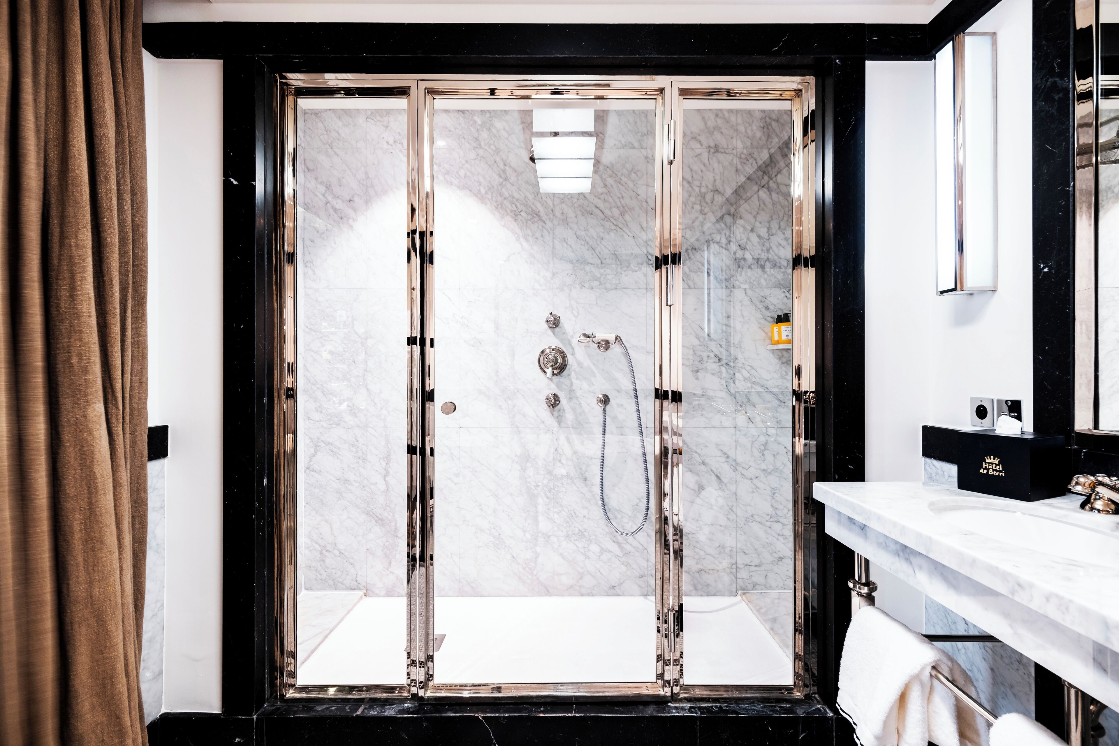 Een moderne badkamer met een douchecabine van glas, marmeren wanden en een witte wastafel met een blad en kastje.