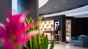 A modern hotel lobby with a bar area, a seating area, and a large potted plant in the foreground. - Mercure Budapest City Center Hotel (Budapest)