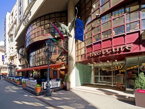 Vista de la calle con un hotel Mercure, mesas al aire libre y un letrero que dice 'Cucina'.