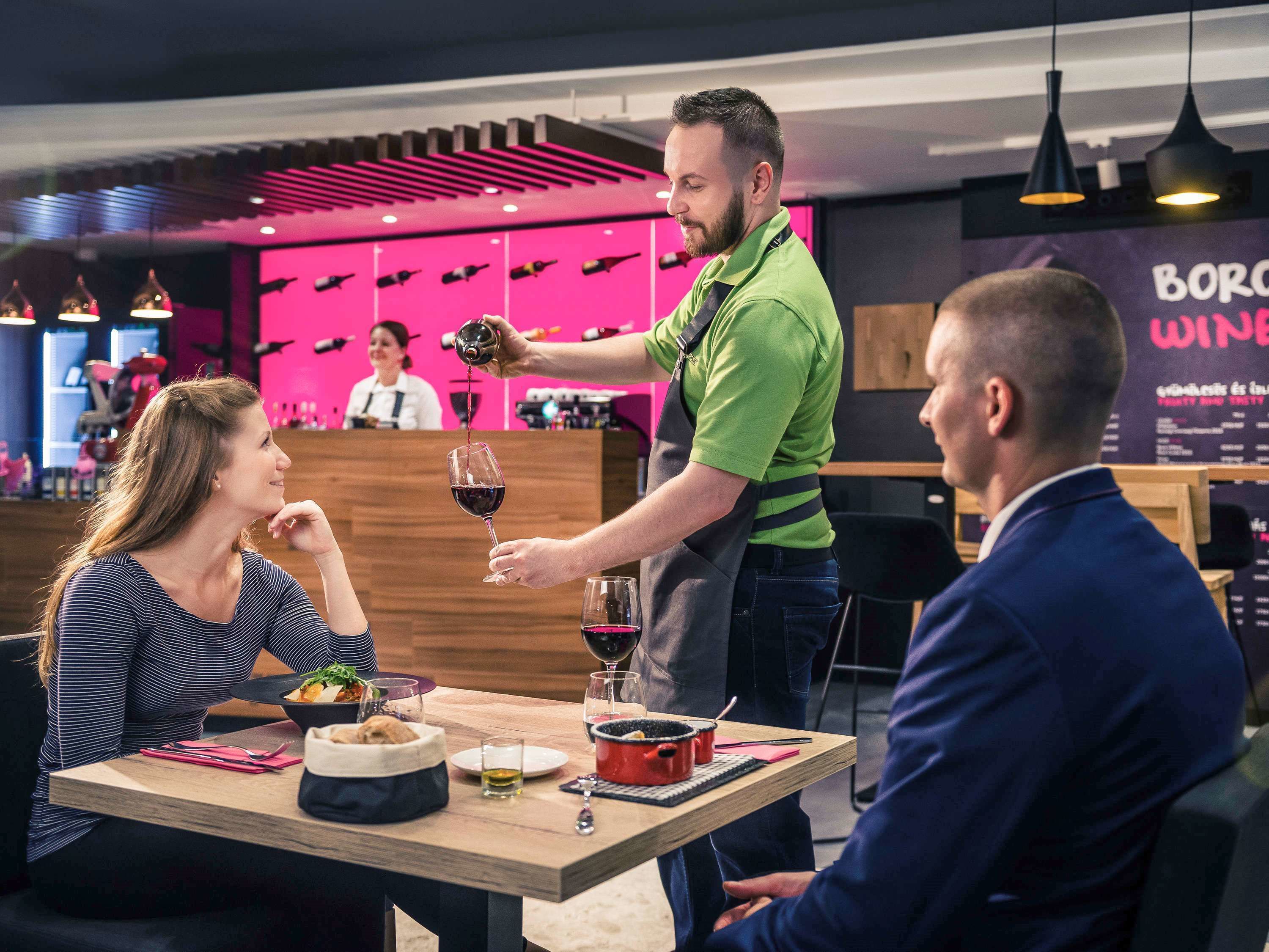 Ein Restaurant mit einem Kellner, der Gästen an einem Tisch Wein serviert.