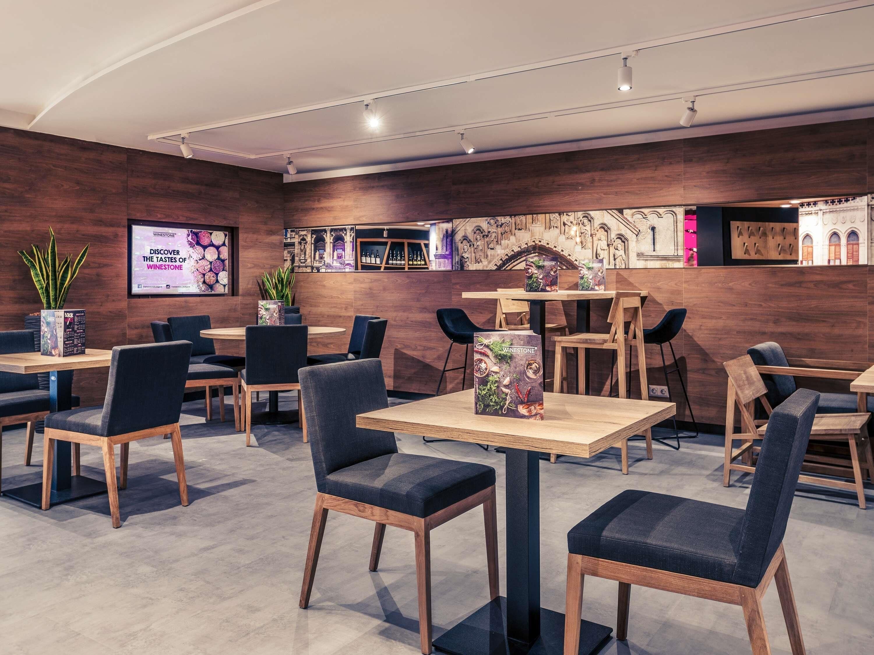 Een modern restaurantinterieur met houten tafels en stoelen, een bar en decoratieve muurkunst.