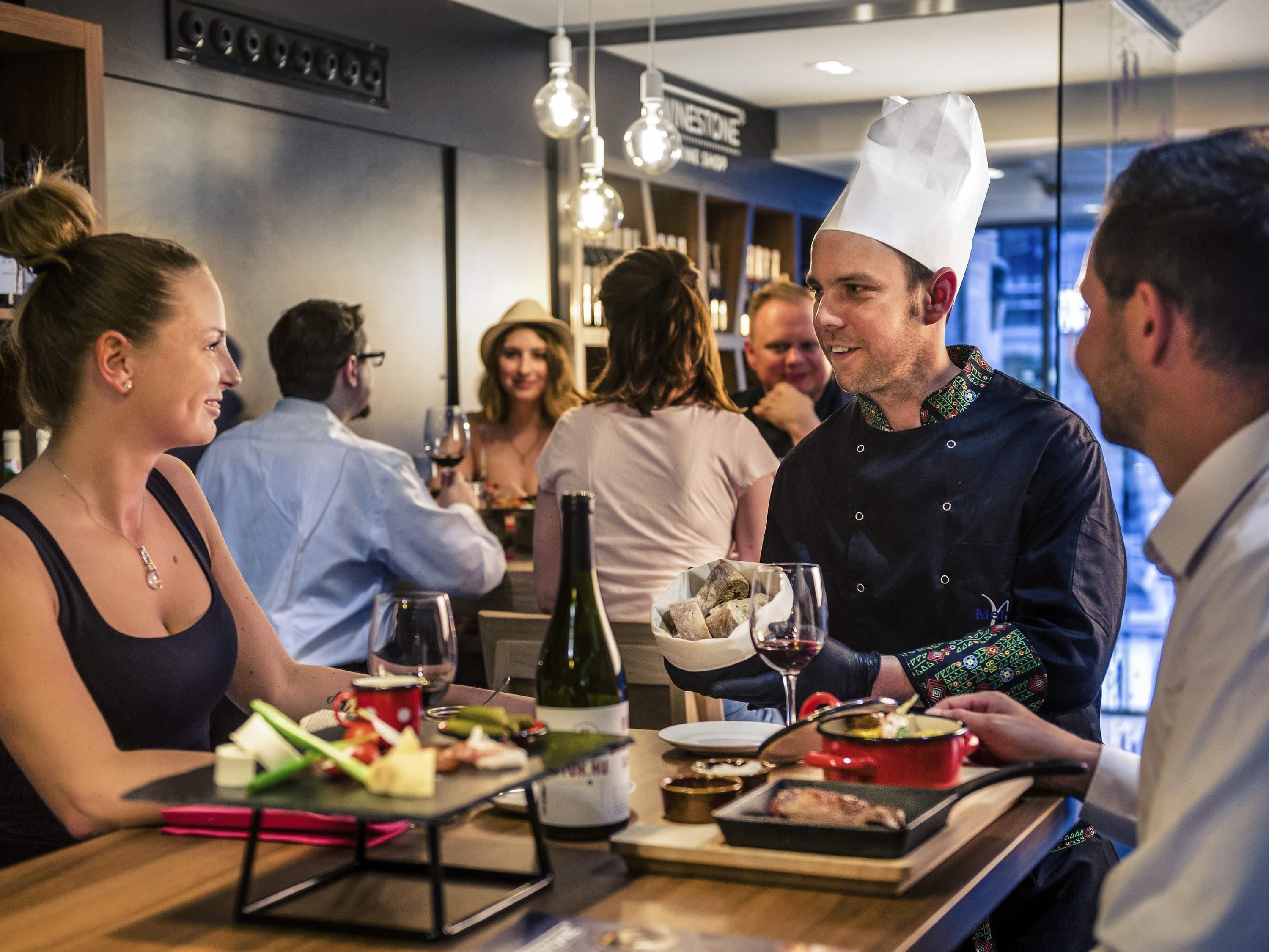 Un gruppo di persone cena in un ristorante con interni moderni, inclusi lampadari e una bottiglia di vino visibile sul tavolo.