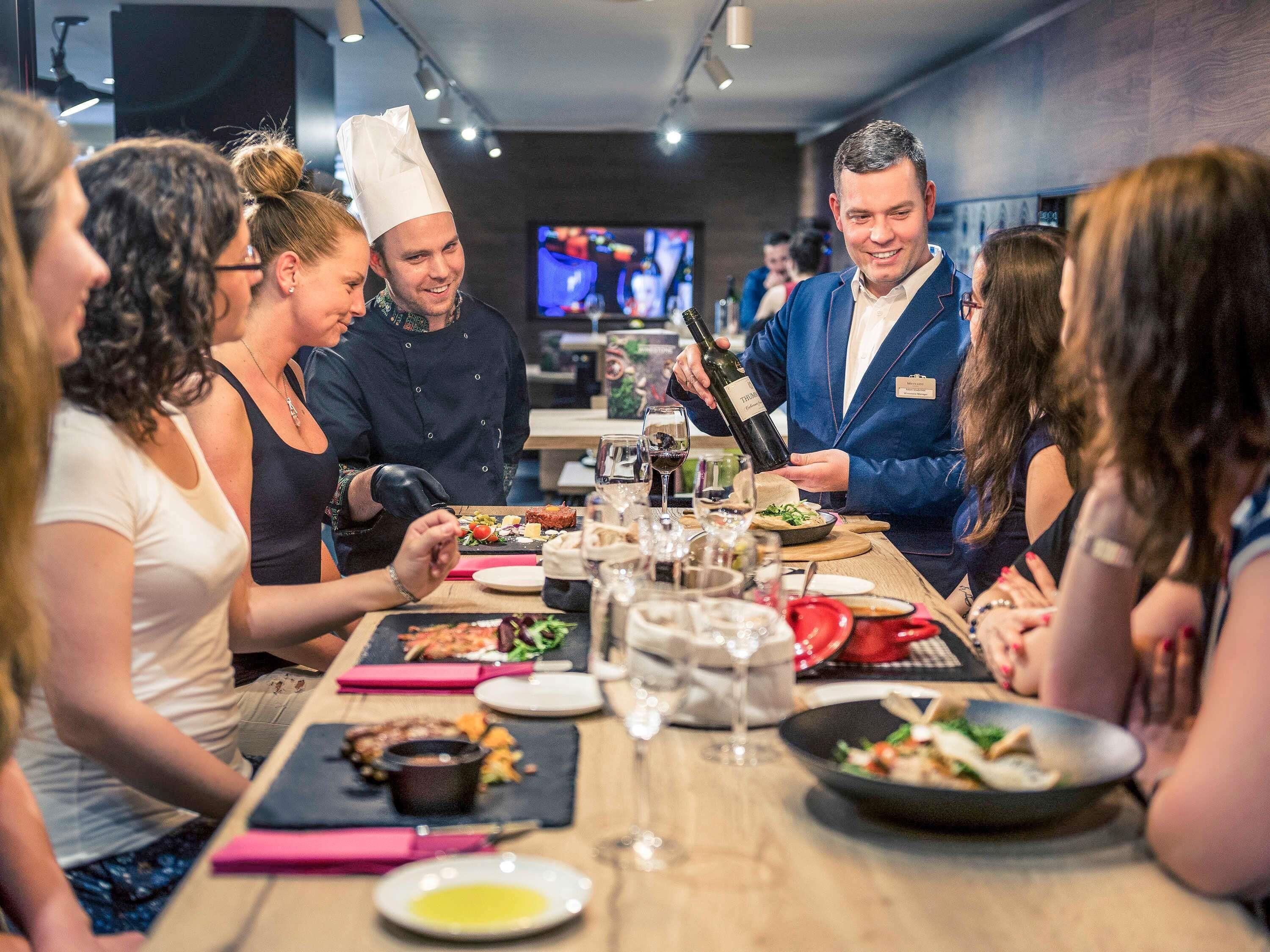 A group of people dining at a restaurant with a long table, various dishes, and a television in the background.
