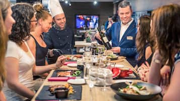 A group of people dining at a restaurant with a long table, various dishes, and a television in the background.