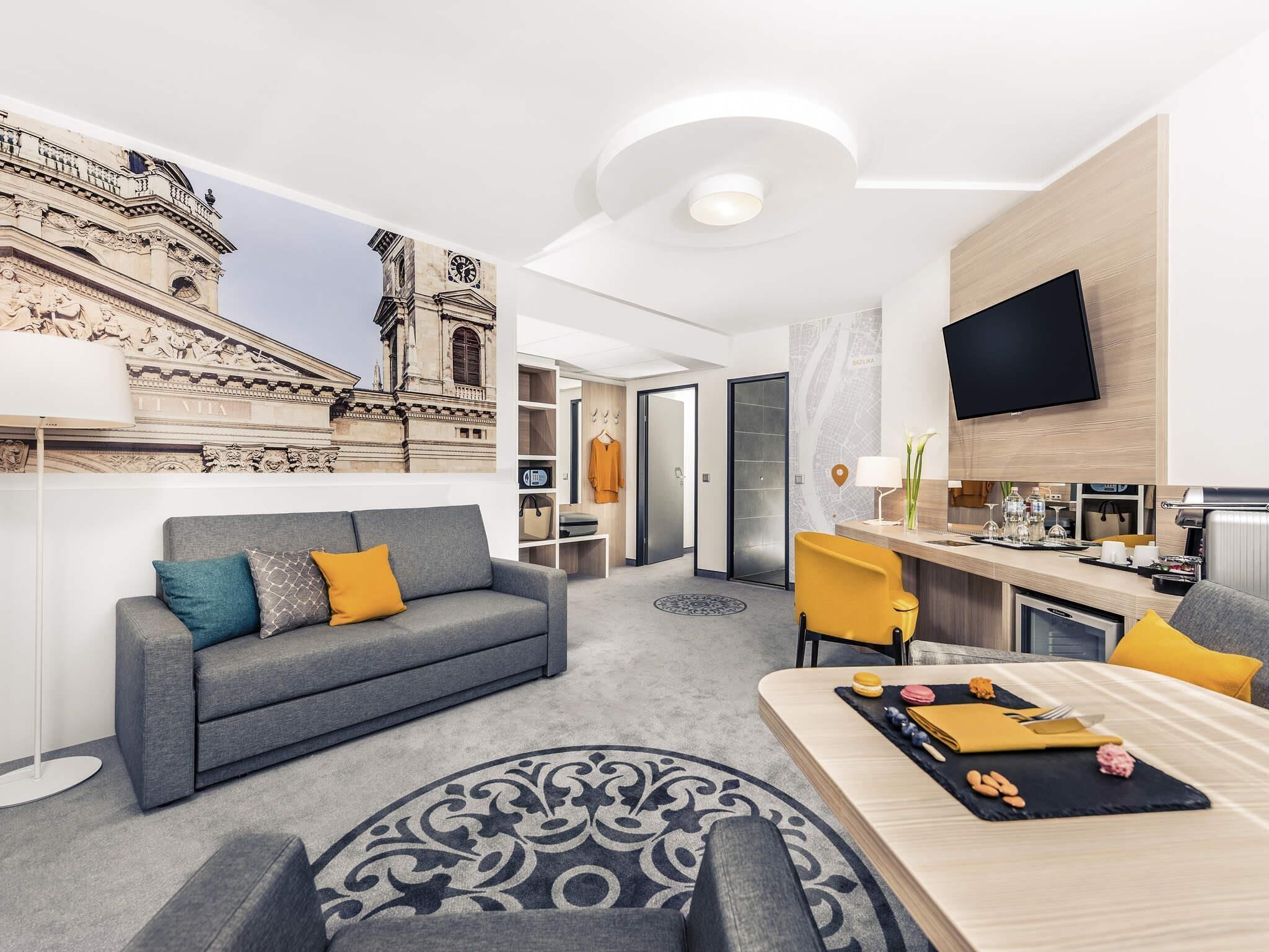 A modern hotel room with a sofa, dining table, and a view of a historic building.