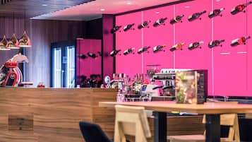 A bar area with a modern design, featuring a pink wall with hanging bottles, a coffee machine, and a variety of liquor bottles.