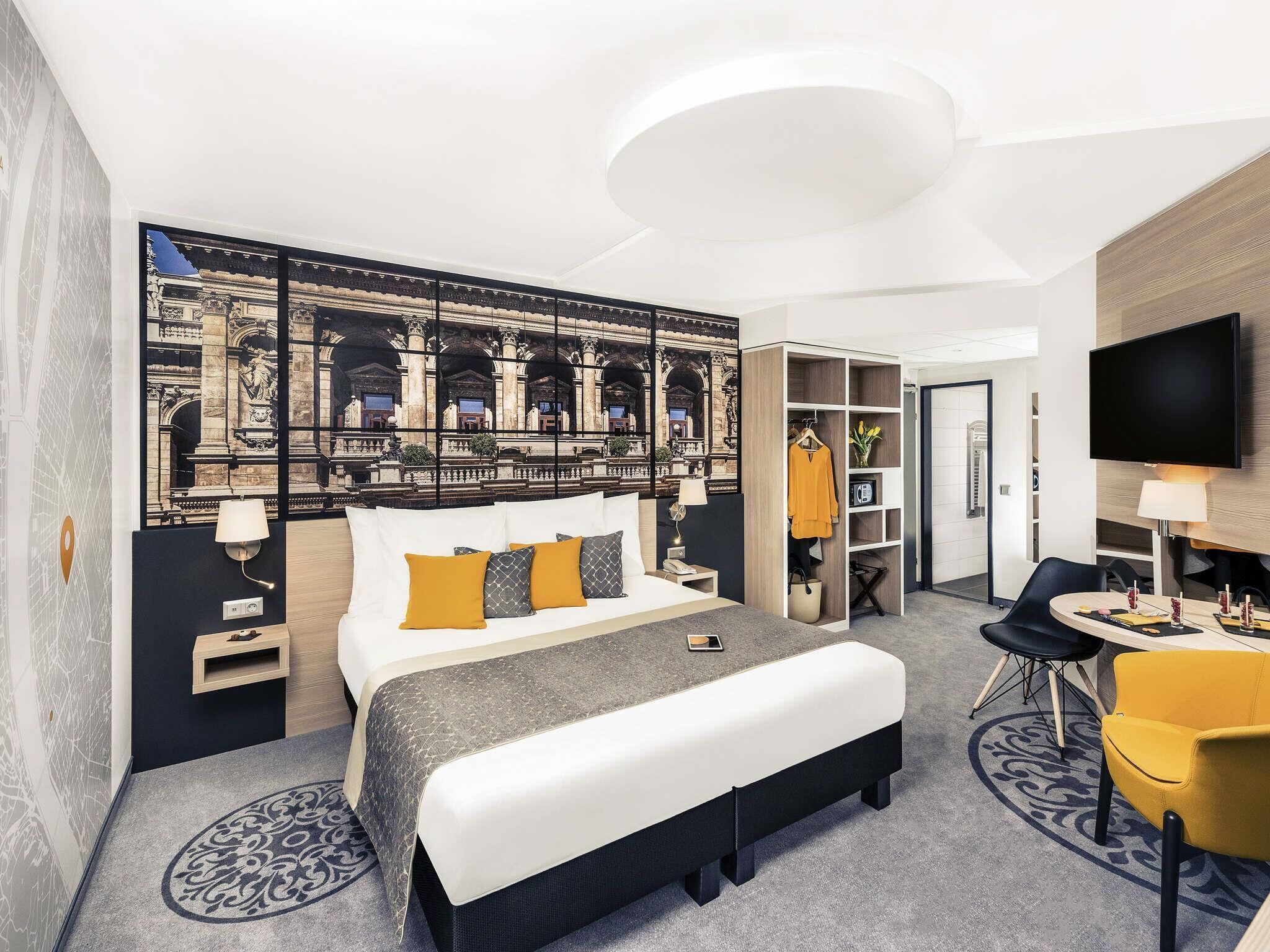A hotel room with a large bed, a desk with a chair, a TV, and a wardrobe.