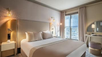 A hotel room with a large bed, a nightstand, a desk, and a view of the city through large windows.