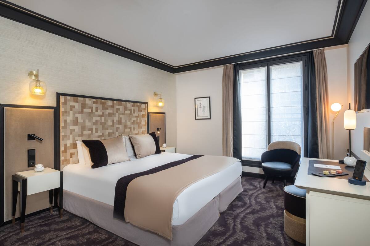 Una habitación de hotel con una cama grande, un escritorio con computadora, una silla y una ventana con cortinas.
