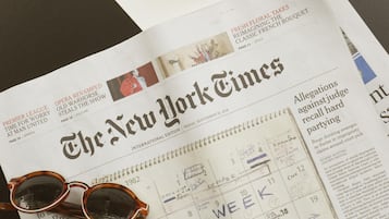 A newspaper with sunglasses on top, a calendar, and a red drink with a garnish.