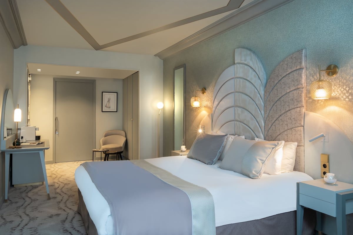 Habitación de hotel con una cama grande, un escritorio, una silla y una lámpara fijada a la pared.