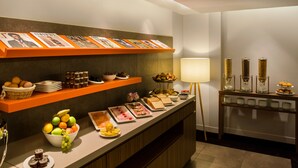 A buffet setup with various food items, a selection of beverages, and informational posters on the wall. - Hôtel Le Derby Alma by Inwood Hotels (Paris)
