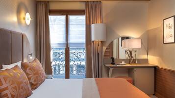 A hotel room with a bed, a desk, a chair, a lamp, and a balcony with a view.