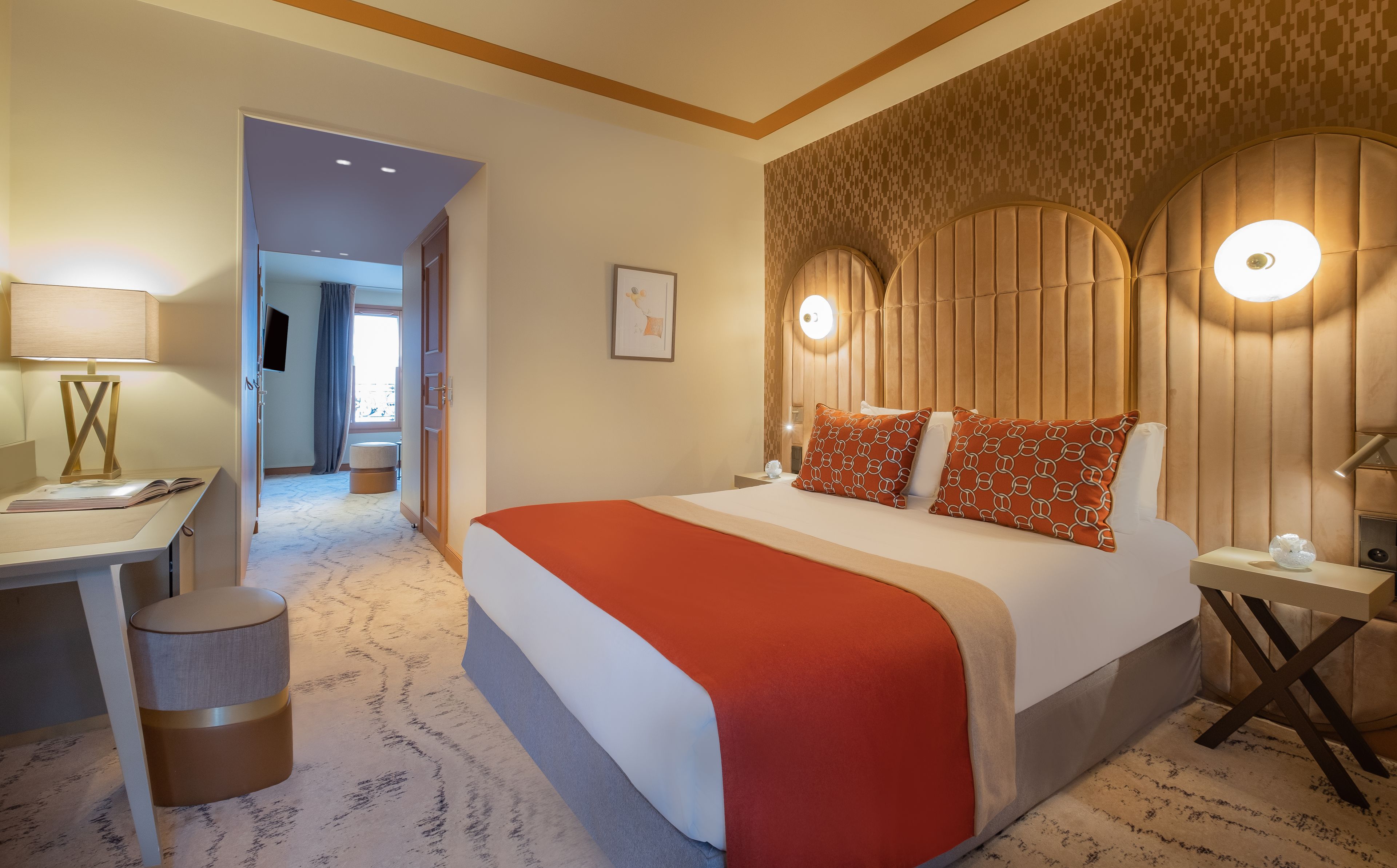 A hotel room with a large bed, a desk with a lamp, a chair, and a small round table.