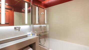 Un baño moderno con ducha envuelta en vidrio, un espejo grande y un revestimiento de baldosas color beige.