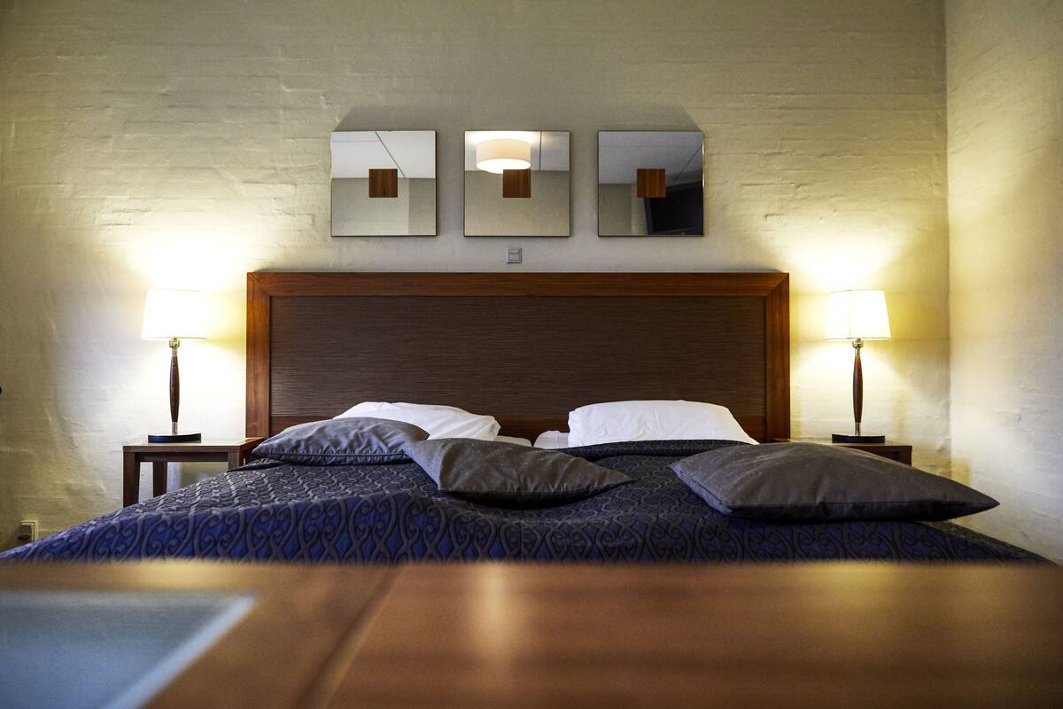 A neatly made bed with a patterned bedspread, two bedside lamps, and three wall-mounted mirrors.