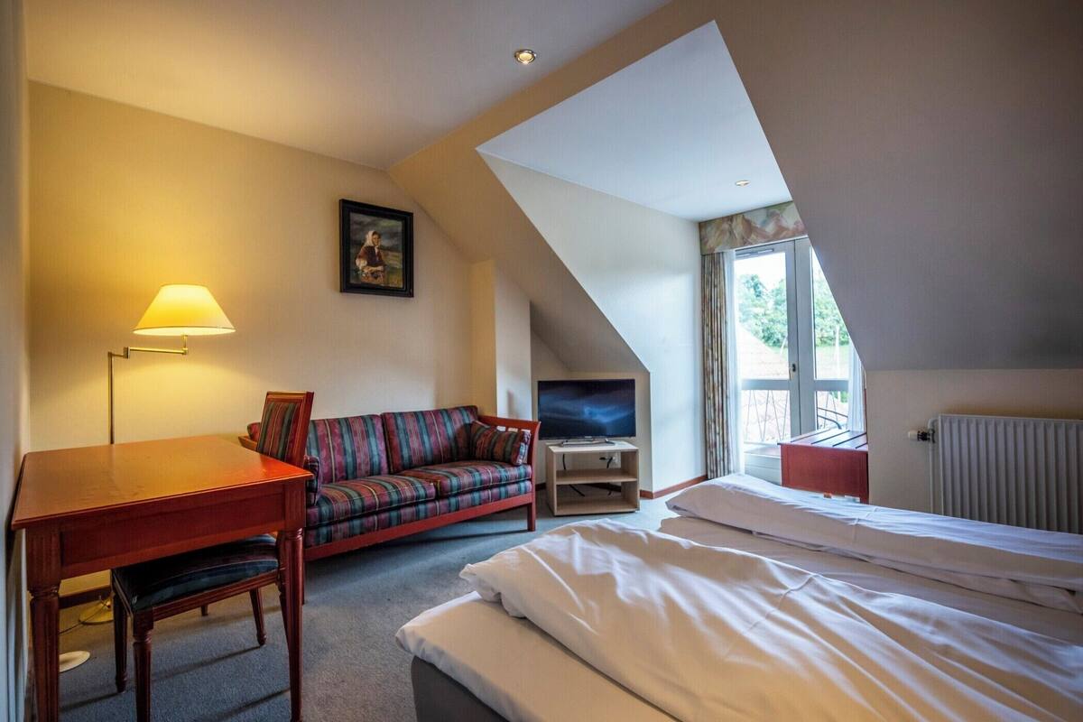 A hotel room with a bed, a sofa, a TV, a lamp, and a window.