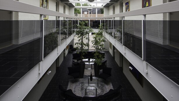 Un atrium modern amb sostre de vidre, paviment negre i una zona d'estar central amb una taula petita i seients.