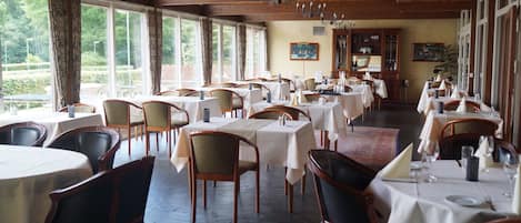 Un restaurante con varias mesas y sillas, amplias ventanas y vigas de madera en el techo.