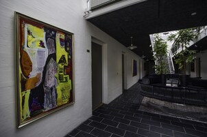Un pasillo con un cuadro abstracto de gran tamaño en la pared, una escalera que sube a un nivel superior y una zona de estar con una valla de metal negro.