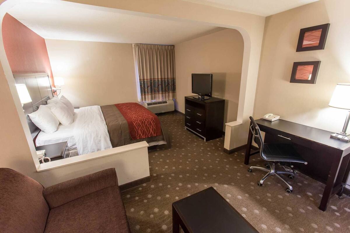 A hotel room with a bed, a desk, a chair, a TV, and a small table.