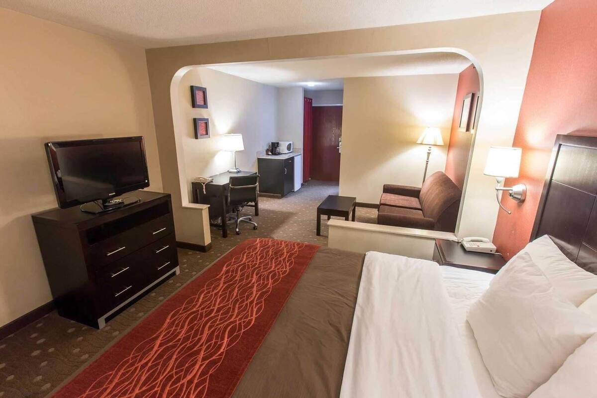 A hotel room with a bed, a TV, a desk with a chair, a lamp, and a small table.