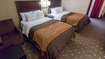 A hotel room with two beds, a brown armchair, a small table, and a carpeted floor.