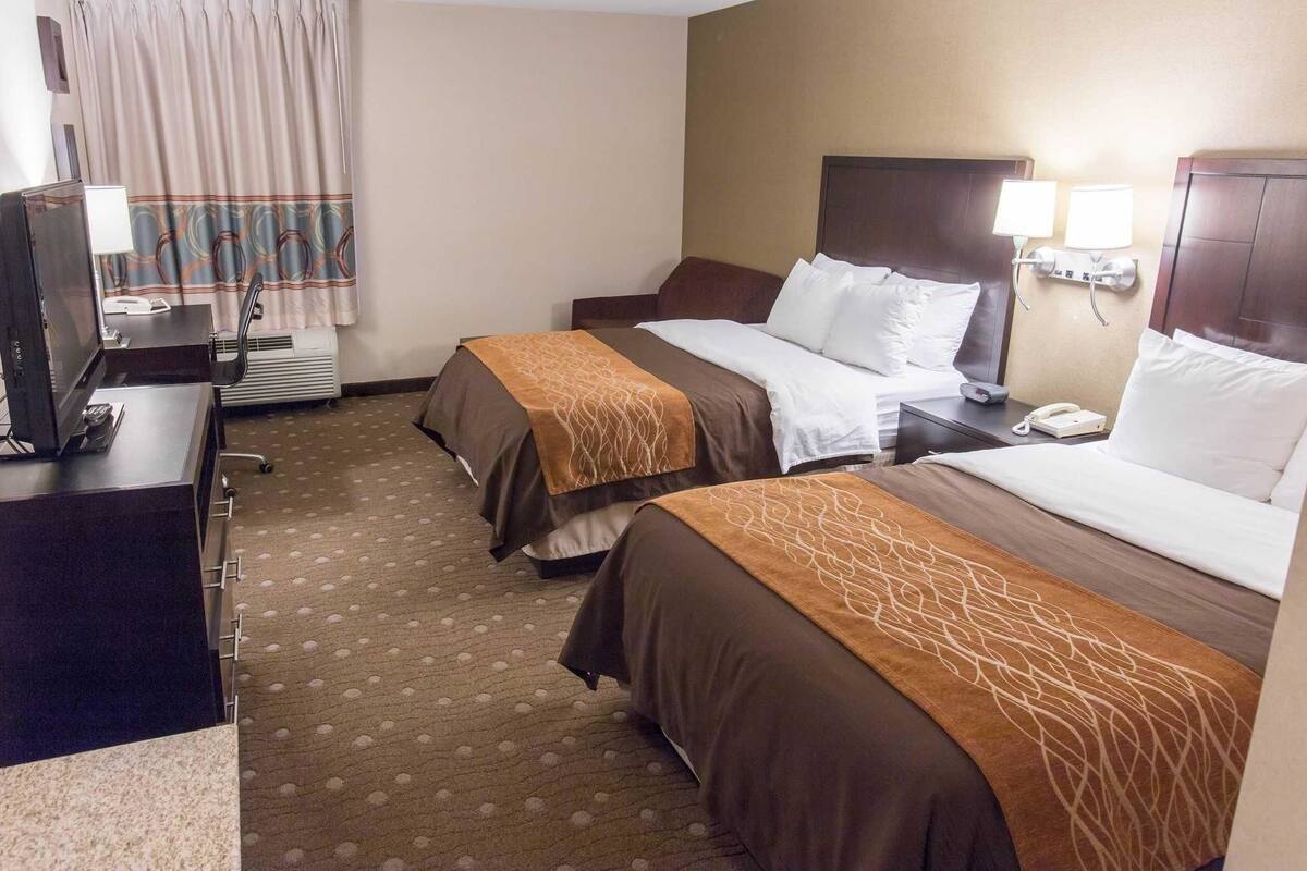 A hotel room with two beds, a desk with a computer, a telephone, and a wall-mounted lamp.
