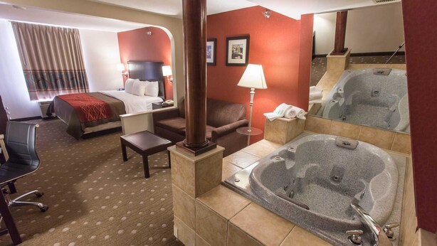 A hotel room with a bed, a desk, a chair, a sofa, a lamp, and a large bathtub. - Comfort Inn Pittsburgh Crafton (Pittsburgh)