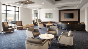 A spacious lounge area with multiple seating options, a large flat-screen TV, and a large window providing natural light. - Courtyard by Marriott Louisville Airport (Louisville)
