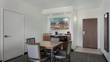 Habitación de hotel con zona de comedor, microondas, lavabo y un cuadro en la pared.