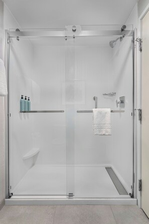 A glass-enclosed shower stall with a white towel hanging on a metal bar, a small shelf with toiletries, and a glass shower door.